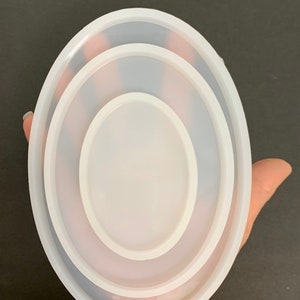 May include: A set of three white oval silicone molds, nested inside each other. The molds are made of flexible silicone and are perfect for creating resin crafts.