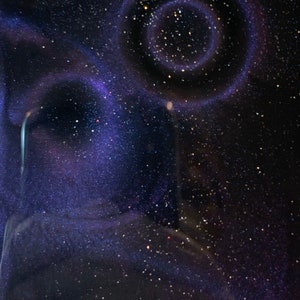 May include: A dark blue phone case with a galaxy design. The case features a swirling nebula effect in shades of purple and blue, with scattered white speckles resembling stars. The case has a camera cutout.