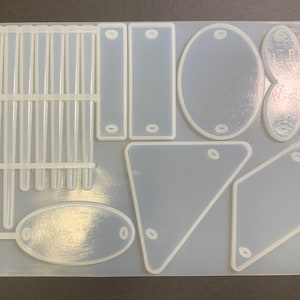 May include: A clear silicone mold with various shapes, including a rectangle, oval, heart, and triangle. The mold is designed for crafting and creating resin jewelry or other decorative items.