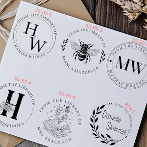 May include: Six different black and white rubber stamps with text that reads "From the Library of" and a name. The stamps are on a white background.