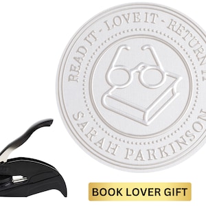 May include: A black self-inking stamp with a white round seal. The seal has the text "READ IT - LOVE IT - RETURN IT" around the edge and "SARAH PARKINSON" at the bottom. Inside the seal is a book with glasses on top. The text "BOOK LOVER GIFT" is in gold letters on a black background.