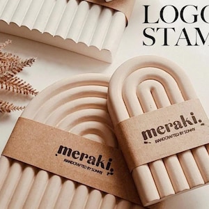 May include: Two light pink, arched, ceramic trays with a raised, textured surface. Each tray has a brown paper label with the text "meraki. handcrafted by sonny" printed in black.