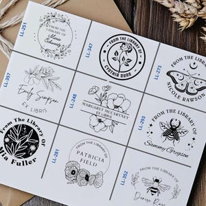 May include: Nine black and white custom bookplate stamps with different designs and names. The stamps feature floral designs, a bee, a butterfly, and a crescent moon.