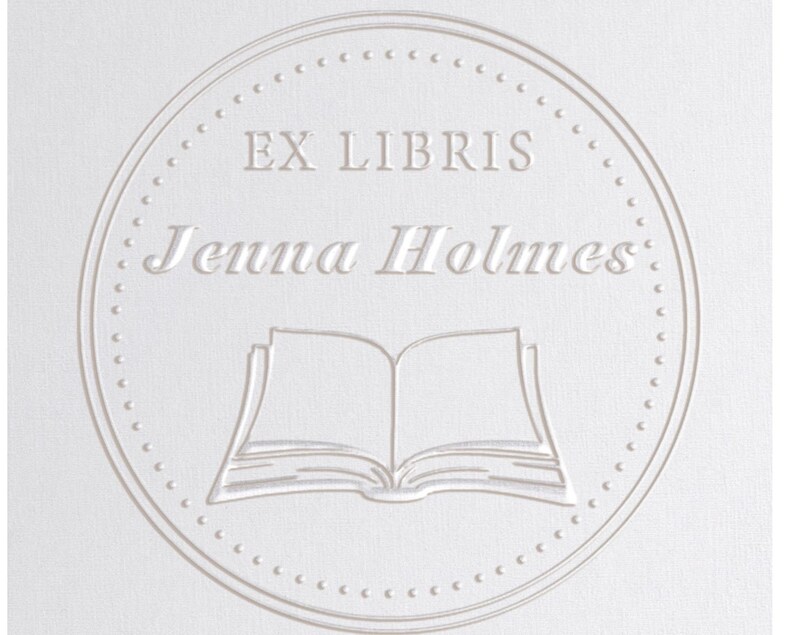 Puede incluir: Un c&iacute;rculo blanco con un borde punteado, que contiene el texto "Ex Libris Jenna Holmes" y una imagen de un libro abierto.