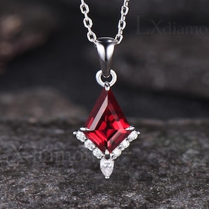 以下が含まれることがあります： 赤い正方形の宝石が、より小さな透明な宝石で囲まれたペンダントが付いた、銀色のチェーンネックレスです。