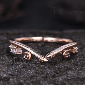 May include: A rose gold V-shaped ring featuring a delicate leaf-inspired band design. The ring is accented with four small, clear round-cut stones set along the sides of the band. The text LXdiamond is visible in the upper right corner.