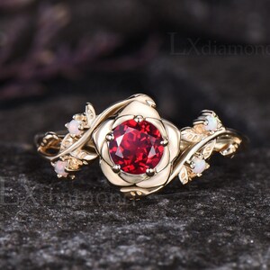 May include: A gold ring featuring a red gemstone set in a rose design. The band is decorated with small white gemstones.