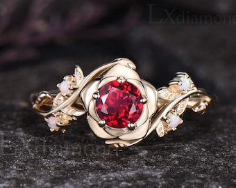 May include: A gold ring with a red gemstone set in a rose-shaped design. The ring is adorned with small white gemstones on the band.