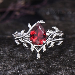 Puede incluir: Un anillo de plata con una piedra roja en forma de pera y un delicado diseño de vid. El anillo está engastado con una sola piedra roja en un engaste en forma de pera.