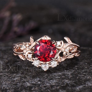 May include: Rose gold ring featuring a large, round, vibrant red gemstone. The ring is adorned with delicate floral and leaf designs, accented with small, sparkling white stones. The intricate details and rich color create an elegant and eye-catching piece of jewelry.