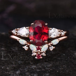 May include: A rose gold engagement ring set with a large oval ruby gemstone surrounded by smaller white gemstones. The band features a delicate floral design with white opals and smaller ruby accents.