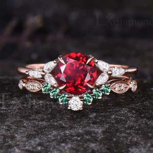 Puede incluir: Un anillo de compromiso de oro rosa con una gran piedra roja rodeada de piedras más pequeñas transparentes y verdes.