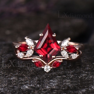 Könnte beinhalten: Ein Ring aus Roségold mit einem großen, roten, quadratischen Edelstein, der von kleineren, weißen Edelsteinen umgeben ist. Der Ring hat ein zartes, florales Design.