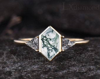 Puede incluir: Anillo de compromiso de oro con una piedra preciosa de ágata verde musgo y dos piedras de acento de diamante negro más pequeñas.