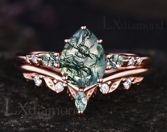 May include: A pear-shaped green moss agate engagement ring set in rose gold with a delicate band of pave diamonds. The ring features a unique and intricate design with a v-shaped band and a floral motif.