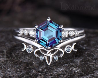 Op de afbeelding: Een zilveren ring met een zeshoekige blauwe edelsteen omringd door kleinere witte edelstenen. De ring heeft een Keltisch knoopontwerp met halve maan accenten.
