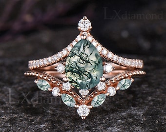 May include: A pear-shaped green moss agate engagement ring set in rose gold with a delicate diamond halo and a matching wedding band. The ring features a unique and intricate design with a delicate floral motif.