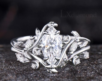 May include: A silver-toned ring featuring a central marquise-cut stone surrounded by a vine-like band with smaller marquise and round stones. The metal band has a polished finish and the text LXdiamond is visible in the upper right corner.
