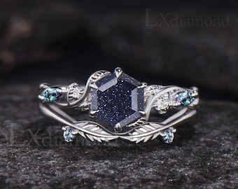 Peut inclure: Une bague en argent sertie d'une pierre précieuse bleue hexagonale entourée de petites pierres blanches. La bande de la bague est décorée d'un motif de feuilles et présente deux petites pierres bleues de chaque côté.