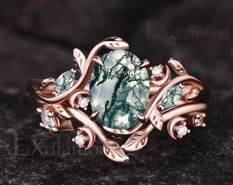 May include: A rose gold engagement ring with a green moss agate oval gemstone surrounded by a delicate vine design with smaller diamonds. The ring is set on a dark background.