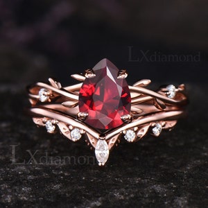 Puede incluir: Un anillo de compromiso de oro rosa con una piedra preciosa roja en forma de pera y un delicado diseño de vid con pequeños diamantes.