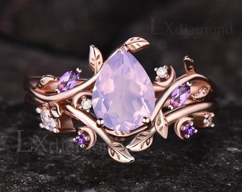 May include: Rose gold ring with a pear-shaped pink gemstone surrounded by smaller purple gemstones and leaves. The ring is set on a white background.