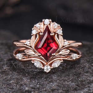 May include: A rose gold engagement ring set with a large, red, square-shaped gemstone surrounded by smaller, clear gemstones. The ring features a delicate floral design.