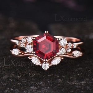 May include: A rose gold engagement ring set with a large, hexagonal, red gemstone surrounded by smaller, round, white gemstones. The ring is set on a black background.