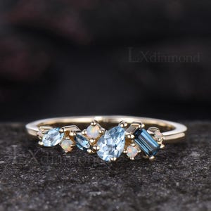 May include: A gold ring featuring a cluster of blue and white gemstones. The ring has a delicate band and is adorned with oval, baguette, and round-cut stones. The gemstones are light blue and white.