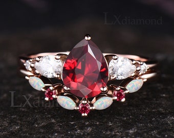 May include: A pear-shaped red gemstone engagement ring set with a matching band. The band features white gemstones and small red gemstones. The ring is set in rose gold.