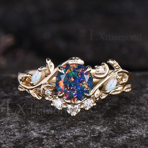 May include: A gold ring featuring an oval, multi-colored opal center stone. The ring has a floral design with small white stones and opal accents. The text "Lxdiamond" is visible in the background.
