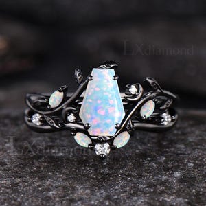 May include: Black ring with a large, light blue, coffin-shaped opal center stone. The ring features a floral design with small white accent stones and leaves. The ring is set against a dark background.