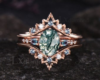 May include: A rose gold engagement ring set with a moss agate center stone and blue topaz accents. The ring features a delicate, intricate design with a crown-like setting.