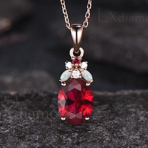 May include: A rose gold necklace with a red oval gemstone pendant surrounded by smaller white and red gemstones.