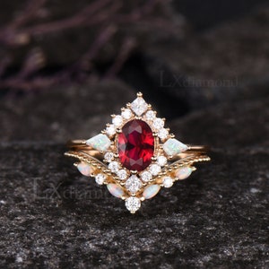 May include: A gold ring set with a large oval red gemstone surrounded by smaller white gemstones. The ring is set with two smaller white gemstones on either side of the main stone. The ring is on a dark gray background.