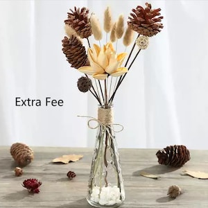 May include: A clear glass vase with a textured surface holds a bouquet of dried flowers. The bouquet includes brown pine cones, dried flower buds, and beige dried flowers. The vase is tied with twine.