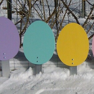 K&ouml;nnte beinhalten: Sieben bunte, ovale Schilder mit wei&szlig;em Hintergrund und einem kleinen Loch in der Mitte. Die Schilder sind auf Metallpfosten montiert und in einer Reihe auf einer schneebedeckten Fl&auml;che angeordnet.