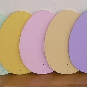 K&ouml;nnte beinhalten: Sieben h&ouml;lzerne Ostereier, die in Pastellfarben bemalt sind: T&uuml;rkis, Hellgr&uuml;n, Gelb, Rosa, Beige, Lavendel und Hellblau.