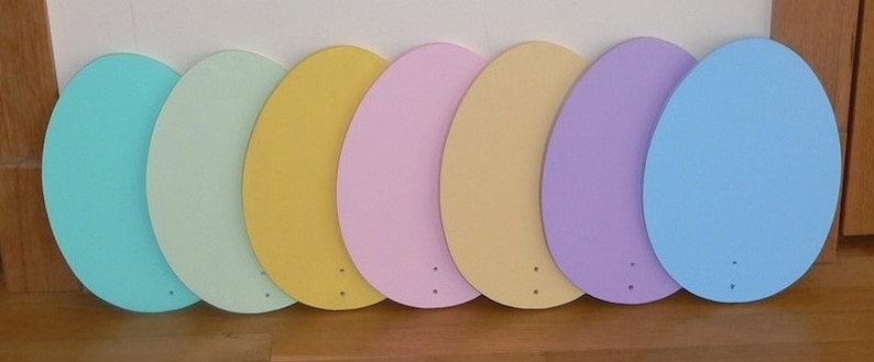 K&ouml;nnte beinhalten: Sieben h&ouml;lzerne Ostereier, die in Pastellfarben bemalt sind: T&uuml;rkis, Hellgr&uuml;n, Gelb, Rosa, Beige, Lavendel und Hellblau.