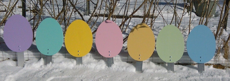 K&ouml;nnte beinhalten: Sieben bunte, ovale Schilder mit wei&szlig;em Hintergrund und einem kleinen Loch in der Mitte. Die Schilder sind auf Metallpfosten montiert und in einer Reihe auf einer schneebedeckten Fl&auml;che angeordnet.