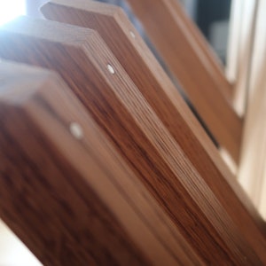 May include: Close-up of multiple wooden slats with a natural wood grain finish. The slats are arranged in a staggered pattern, creating a visual texture. The slats are secured together with small, white metal fasteners.