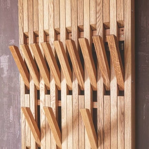 May include: A wooden wall-mounted coat rack with multiple hooks. The hooks are made of wood and are arranged in a staggered pattern. The rack is made of natural wood and has a light brown finish.