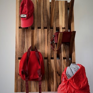 Può includere: Un appendiabiti da parete in legno con più ganci. L'appendiabiti ha un cappello rosso, uno zaino rosso, due borse rosse e una giacca rossa appese.