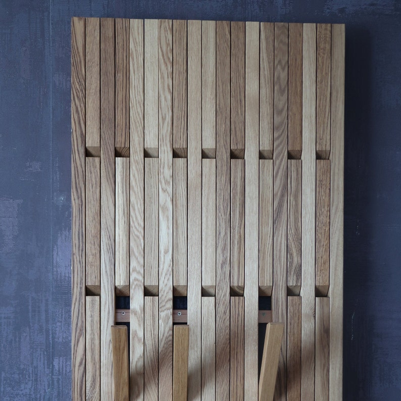 May include: A wooden wall-mounted coat rack with a slatted design. The rack has multiple slots for hanging coats, hats, or bags.
