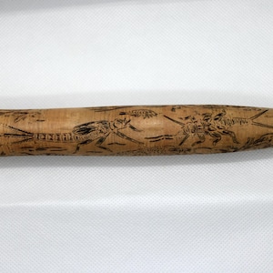 Puede incluir: Objeto cilíndrico de madera con diseños de insectos grabados. La madera de color marrón claro está decorada con ilustraciones negras detalladas de varios insectos y follaje. El objeto tiene un extremo redondeado y una base más ancha, lo que sugiere un mango o herramienta.