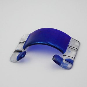 May include: A blue glass phone holder with white and black stripes. The holder is shaped like a curved arch.