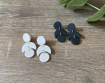 May include: A pair of white and black geometric dangle earrings. The earrings are made of polymer clay and feature a crescent moon shape with a circle at the bottom.