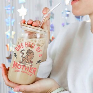 May include: A clear glass jar with a bamboo lid and a straw. The jar has a graphic of a tiger with the text "One Hell of a Mother Feral Moms Club".
