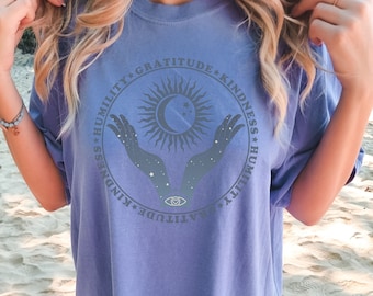 May include: A purple oversized t-shirt with a graphic of a sun and moon with hands reaching up. The graphic is surrounded by the words "Humility, Gratitude, Kindness".