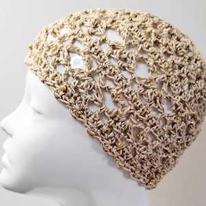 May include: A beige crochet hat with gold glitter and beads. The hat is made with a delicate openwork pattern.